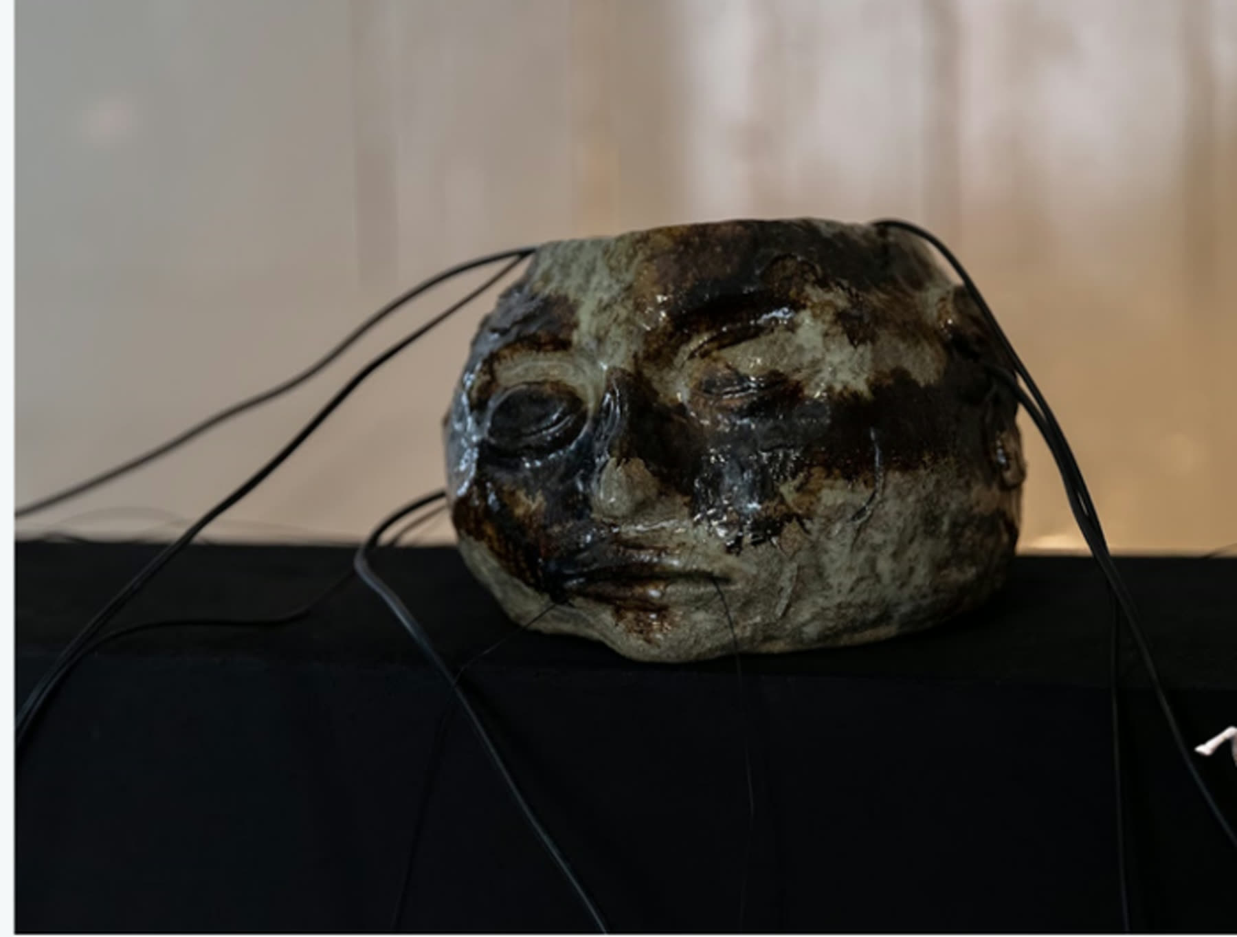 A ceramic sculpted face with sensor wires trailing from it, resting on a dark surface.