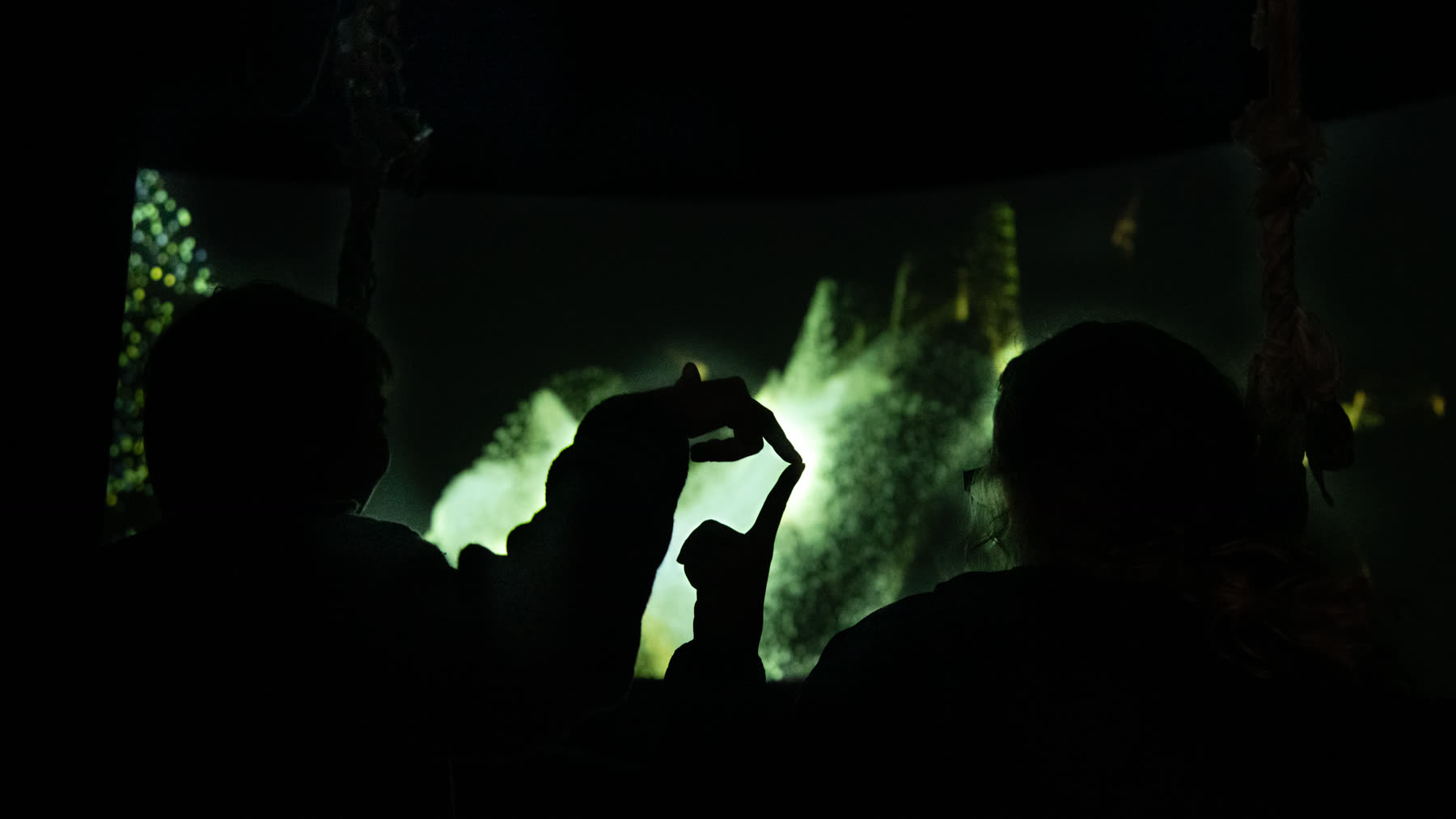 Visitors silhouetted against an immersive green projection, a hand reaching up into the light.